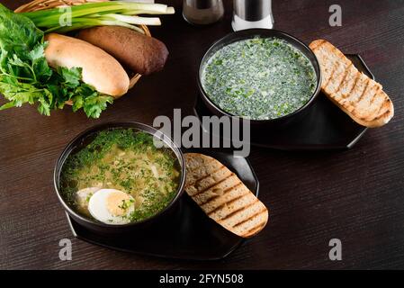 Okroshka, bouillon avec nouilles et œufs dans une assiette noire, pain grillé, herbes sur une table en bois sombre. Déjeuner de saison sain Banque D'Images