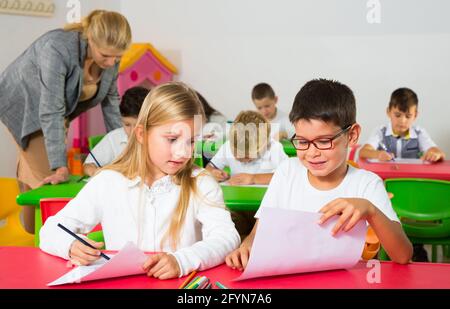 Les élèves heureux assis bavardant à leçon à l'école élémentaire Banque D'Images