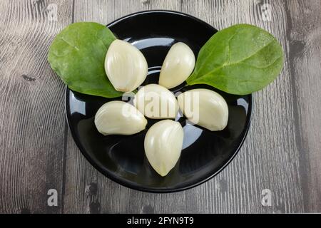 Têtes d'ail pelé naturel et feuilles de laitue sur un plaque noire Banque D'Images