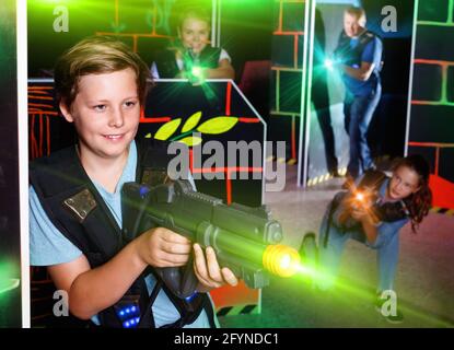 Heureux happy smiling boy positives visant pistolet laser à d'autres joueurs pendant le jeu laser tag in dark room Banque D'Images