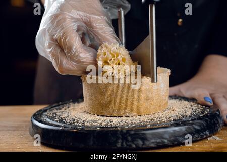 Rasage de la tête de moine à l'aide d'un couteau à girofle. Tête de moines. Variété de fromage semi-dur suisse à base de lait de vache. Banque D'Images