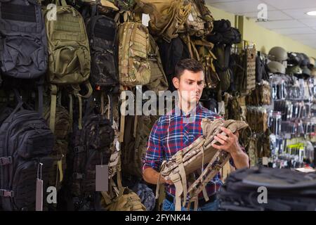 positif homme choisissant le pistolet textile sac à dos dans la boutique militaire Banque D'Images