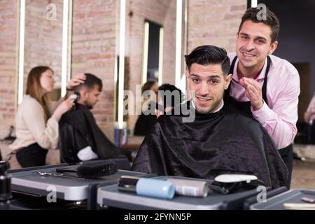 Portrait de main-d'hairstylist et satisfait la clientèle masculine après coupe de cheveux moderne en studio Banque D'Images