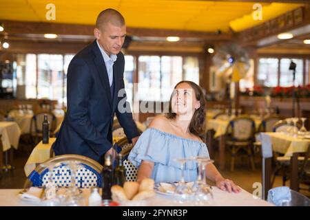 Gentilhomme aidant jeune femme attrayante avec sa chaise dans le restaurant Banque D'Images