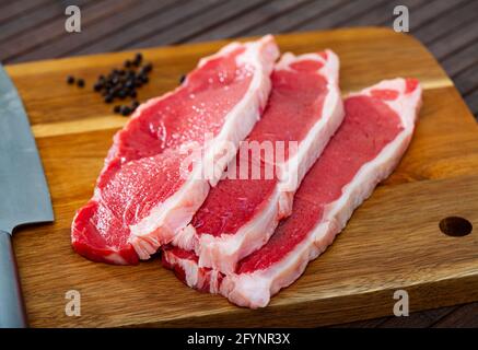 Ingrédients pour la cuisson. Entrecotes de bœuf cru avec du poivre sur une surface en bois Banque D'Images