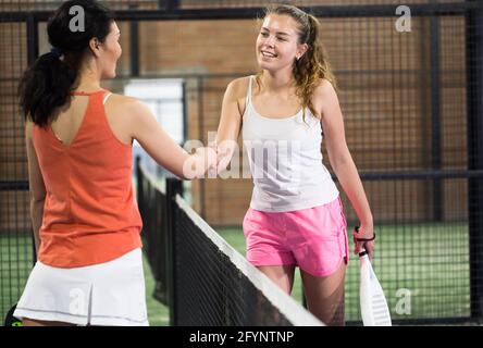 Jeune femme souriante joueur de padel poignée de main après avoir joué à un match sur le terrain Banque D'Images