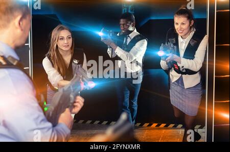 Groupe de collègues souriants et agréables et satisfaits tenant des pistolets laser jouant au jeu de tags laser Banque D'Images