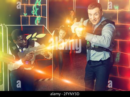 Groupe de collègues souriants et joyeux tenant des pistolets laser jouant au jeu de tags laser Banque D'Images