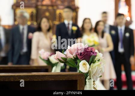 Fleurs roses décoratives avec fond flou de mariée, de marié, d'amis et de parents à l'église lors d'une cérémonie de mariage Banque D'Images