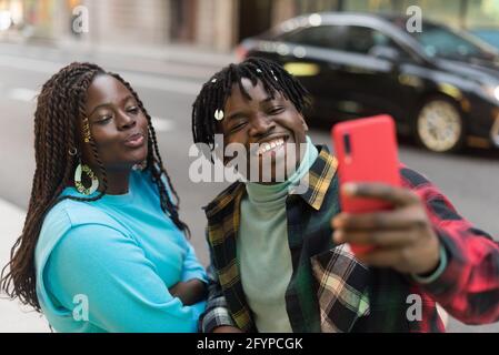 Un couple noir souriant prend un selfie dans la rue. Banque D'Images