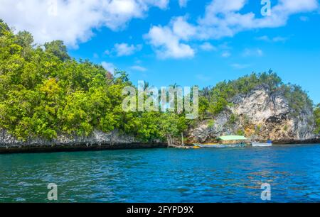 Côte d'une île tropicale rocheuse par une journée ensoleillée. Petite jetée et bateaux. Toits d'un petit village en épaists parmi les palmiers Banque D'Images