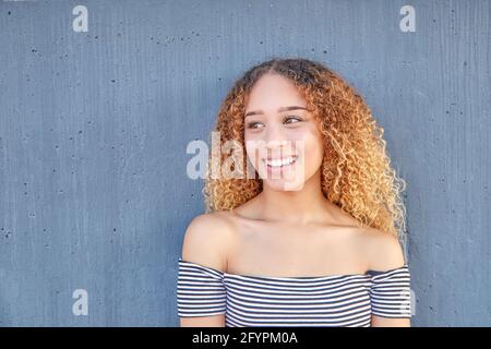 Portrait souriant de l'adolescent de Latina sur fond gris. Gros plan de la jeune fille avec des cheveux bouclés heureux. Photo de haute qualité Banque D'Images