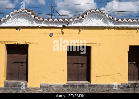 Détail de l'avant d'un bâtiment à Antigua Guatemala avec des toits ornés de style, des murs peints en jaune et des portes en fer. Banque D'Images