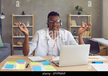 Un homme afro-américain décontracté écoute de la musique dans un casque et médite lorsqu'il est assis au travail. Banque D'Images