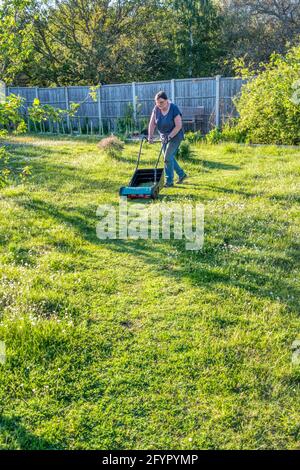 Femme laissant l'herbe pousser plus longtemps dans le jardin pour No Mow May et juste en coupant un court chemin à travers elle. Permet aux fleurs sauvages de fleurir et aide les insectes. Banque D'Images