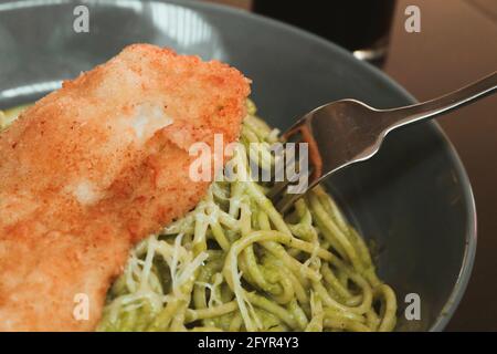 Gros plan sur les appétissantes pâtes au pesto avec du parmesan et du filet croustillant de poulet sur le dessus Banque D'Images