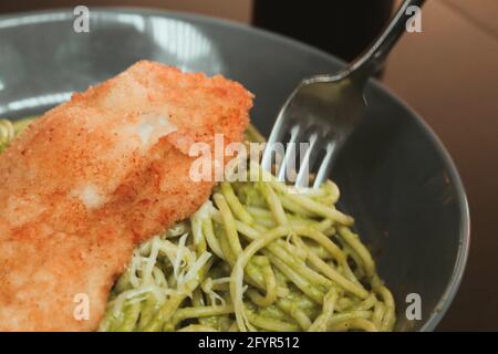 Gros plan sur les appétissantes pâtes au pesto avec du parmesan et du filet croustillant de poulet sur le dessus Banque D'Images