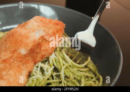 Gros plan sur les appétissantes pâtes au pesto avec du parmesan et du filet croustillant de poulet sur le dessus Banque D'Images