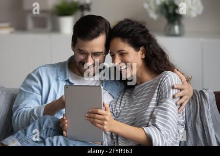 Un couple multiethnique souriant utilise une tablette moderne à la maison Banque D'Images