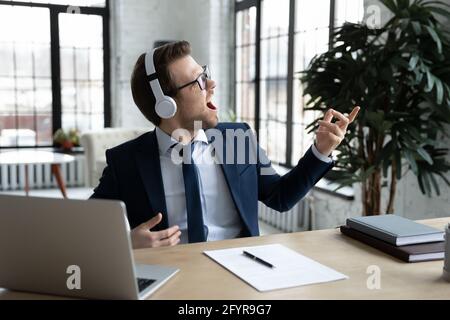 Joyeux homme d'affaires amusant dans des écouteurs sans fil écoutant de la musique Banque D'Images