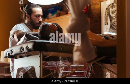 Voir sous de tatouage artiste travaillant avec un client dans son studio. Banque D'Images