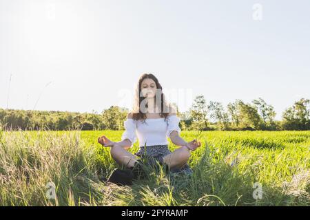 femme méditant au milieu d'un champ de blé vert contre le soleil Banque D'Images