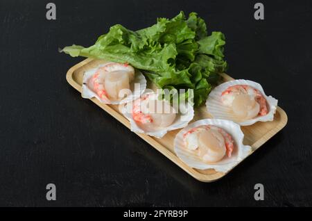 Un pétoncle brut naturel avec une queue de crevettes dans la coquille avec une feuille de laitue dans un bol en bois sur fond sombre. Mise au point sélective. Banque D'Images