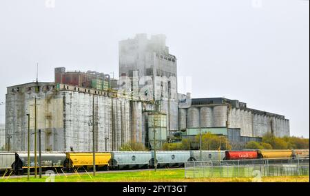 Lors d'une journée de printemps brumeux, les wagons pleins de grain apportent leurs charges de grain aux silos à grains pour être entreposés et expédiés vers les marchés du monde entier. Banque D'Images