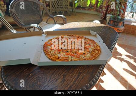 Grande pizza dans une boîte en carton sur une table en bois. Banque D'Images
