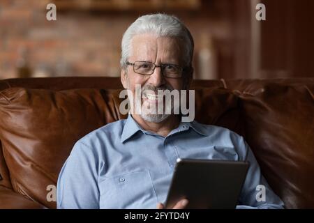 Un homme plus âgé décontracté s'assoit sur un canapé à la maison avec une tablette Banque D'Images
