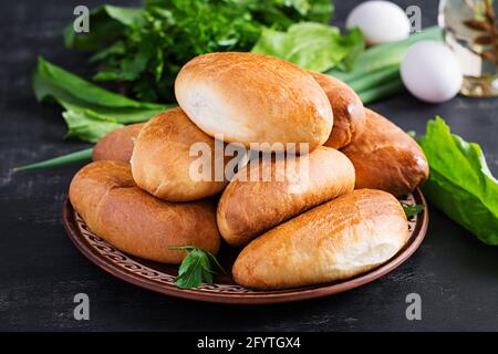 Tartes ukrainiennes traditionnelles avec œufs, oignon vert, sorrel sur fond sombre. Piroshki russe, viandes cuites maison. Banque D'Images