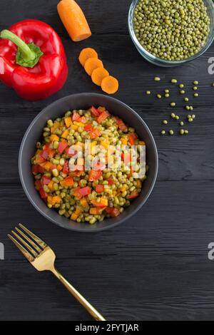 Munter les haricots avec les légumes dans le bol sur le fond en bois noir. Emplacement vertical. Banque D'Images