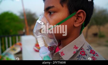 Un petit garçon qui respire avec un masque à oxygène à la maison. Enfant indien malade infecté par la maladie de Covid 19. Garçon indien prenant traitement de l'asthme, poumons. Banque D'Images