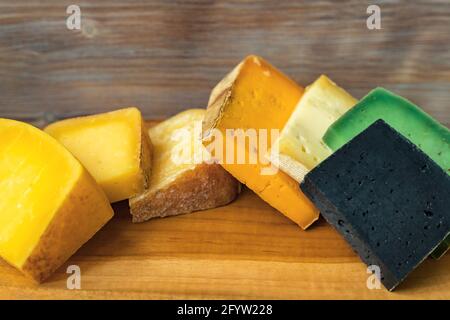 Planche à découper en bois avec des morceaux de différentes couleurs de fromage sur fond de mur en bois Banque D'Images