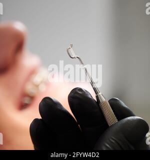 Marco instantané de l'outil dentaire en acier tenu par les mains du dentiste dans un gant en latex noir. Le ruban en caoutchouc blanc pour les bretelles est sur l'outil. Mise au point sélective. Le sourire de l'homme sur un arrière-plan flou Banque D'Images