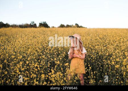 Élégant bébé fille 4-5 ans porter jaune robe élégante et chapeau de paille dans fleur champ sur la nature fond gros plan. Saison des vacances d'été. Banque D'Images