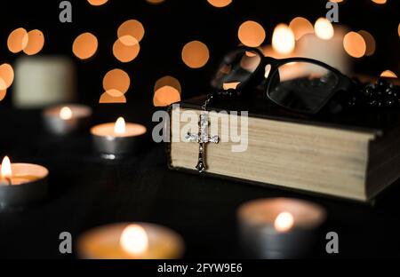 Rosary sur la sainte bible avec des bougies et des lumières de bokeh arrière-plan. Banque D'Images