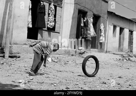 Village de Hawzien (région du Tigré), Éthiopie - septembre 2011 : enfant éthiopien jouant avec un vieux pneu devant les magasins locaux vendant des robes. Banque D'Images