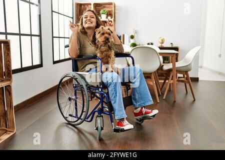 Jeune fille hispanique assise en fauteuil roulant à la maison avec une expression triste couvrant le visage avec les mains en pleurant. Concept de dépression. Banque D'Images