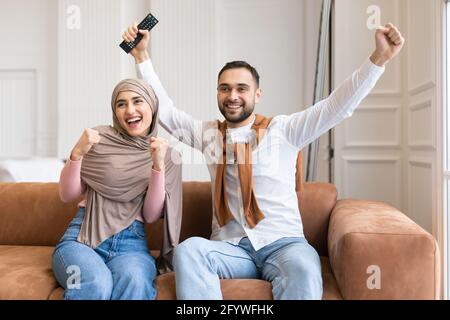 Couple musulman émotionnel secouant les poings devant la télévision à la maison Banque D'Images