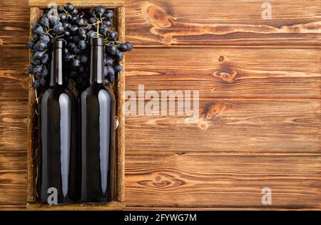 Composition de deux bouteilles de vin rouge sur une table en bois brun. Bouteilles de vin rouge en boîte sur des raisins mûrs noirs sur une table en bois. Ancienne étiquette de vin de collection Banque D'Images