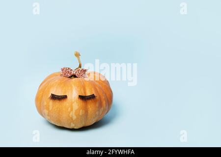 Citrouille avec faux cils et noeud rose sur fond bleu. Automne, automne, halloween concept. Espace de copie Banque D'Images