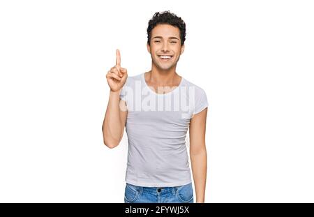 Jeune homme beau portant décontracté t-shirt blanc pointant le doigt vers le haut avec une idée réussie. Sorti et heureux. Numéro un. Banque D'Images
