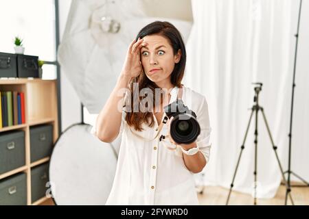 Belle femme caucasienne travaillant comme photographe au studio de photographie inquiet et stressé au sujet d'un problème de main sur le front, nerveux et anxiou Banque D'Images