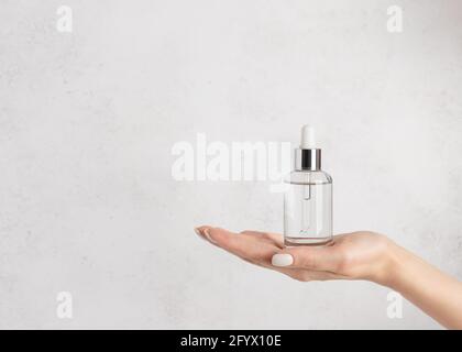 main de femme tenant un flacon en verre avec du sérum hydratant. Beauté cosmétique concept de soin de la peau. Fond blanc en béton. Image horizontale Banque D'Images