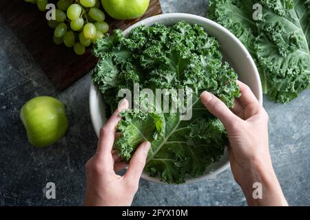 Les mains des femmes lavant le chou kale dans un bol d'eau. Cuisine saine bio maison de la nourriture végétalienne, vue de dessus Banque D'Images