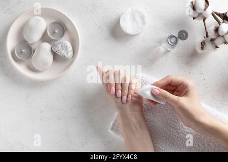 jeune femme enlevant vernis à ongles rose avec le liquide dissolvant. Concept d'hygiène et de soins personnels. Fond blanc en béton, plat. Banque D'Images