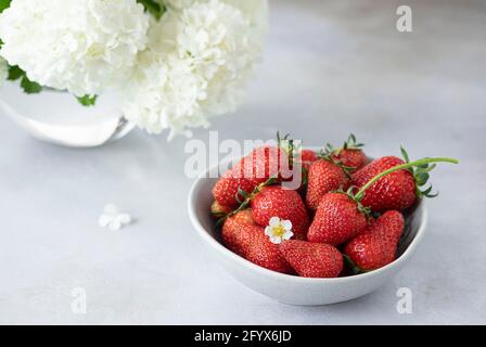 bol avec fraises fraîches et beau bouquet de fleurs blanches. nourriture saine en vitamines. espace copie. Arrière-plan gris. Banque D'Images