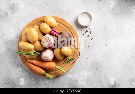 assortiment de légumes frais sur planche à découper ronde en bois. pommes de terre pour bébés, betteraves, carottes, ail, romarin Banque D'Images