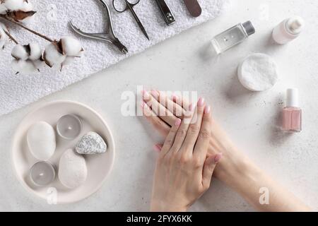 mains de femme avec manucure rose délicate sur le fond des outils de manucure. salon de ongles et spa. Arrière-plan blanc en béton, vue du dessus. Banque D'Images